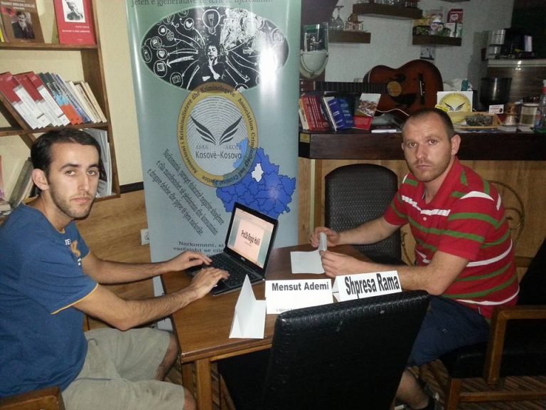 Dy persona pranë një tavoline pune me laptop.