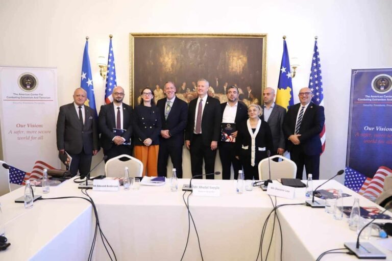 Grup pjesëmarrësish pas një tavoline me mikrofona.